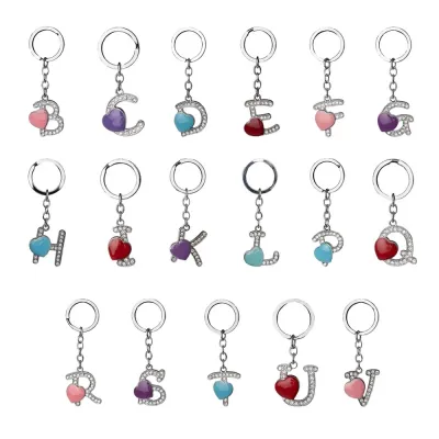 Chaveiro de metal, formato de letra, com pedras brilhantes e detalhe em coração.
